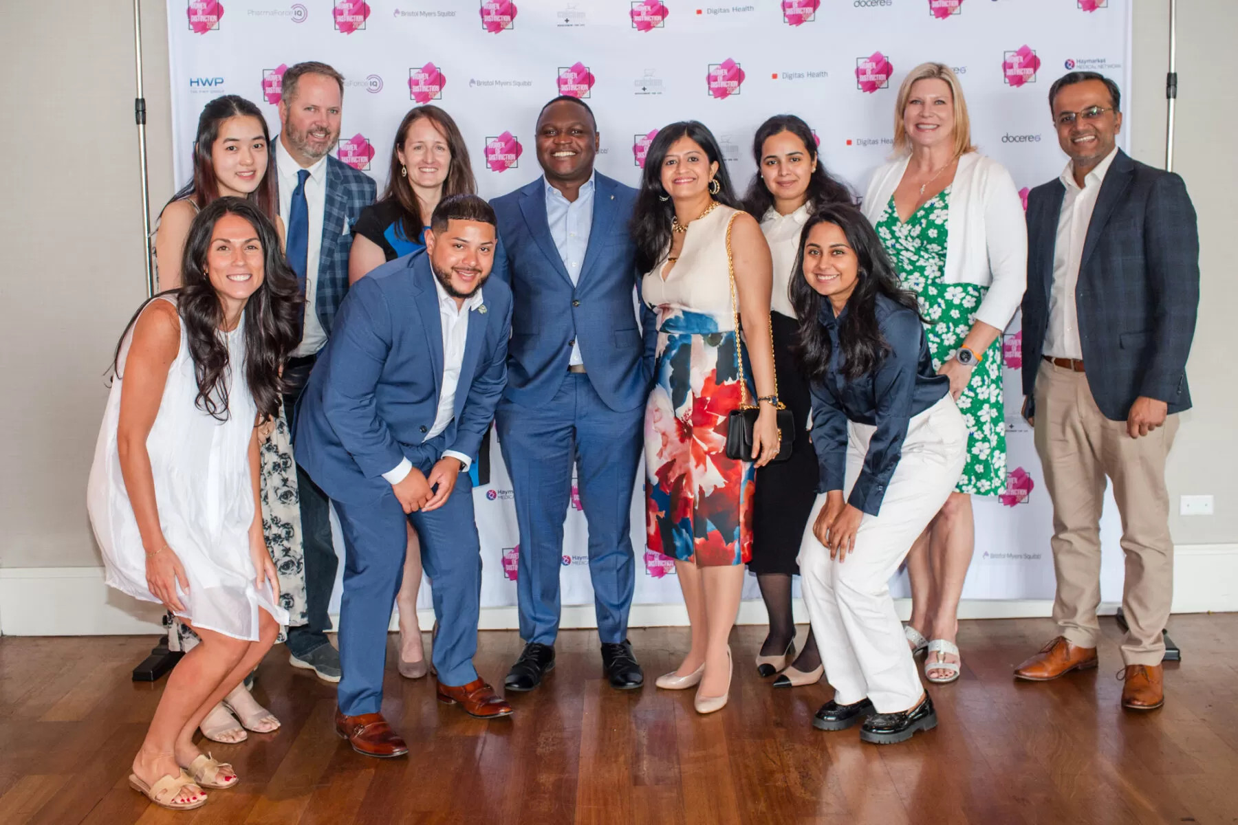 Photo of a group of men and women at a business event in front of logos on a step and repeat
