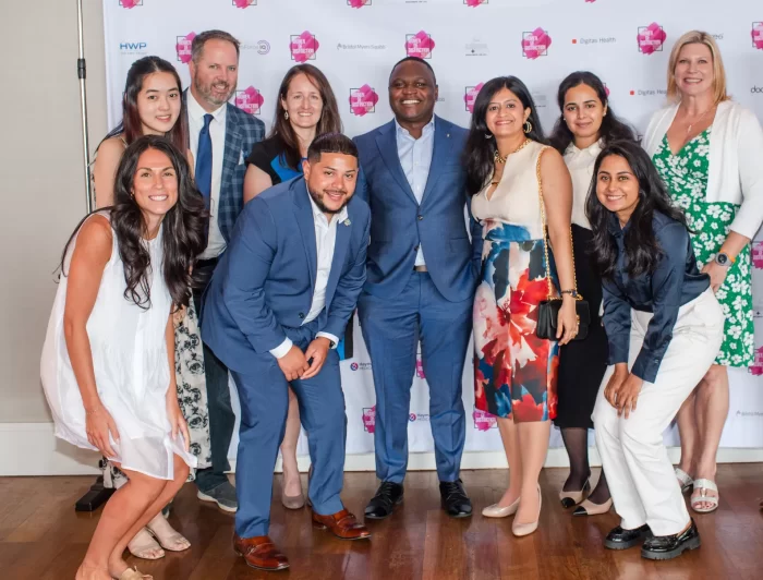 Photo of a group of men and women at a business event in front of logos on a step and repeat
